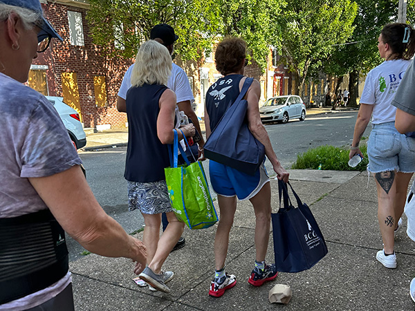 People with bags walking down the sidewalk.